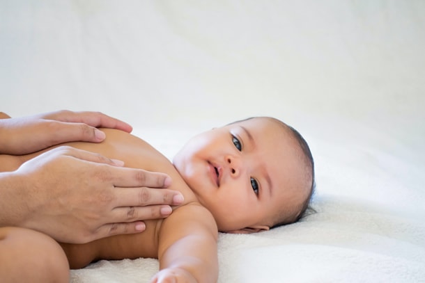 Ein nacktes Baby wird auf dem Rücken liegend massiert